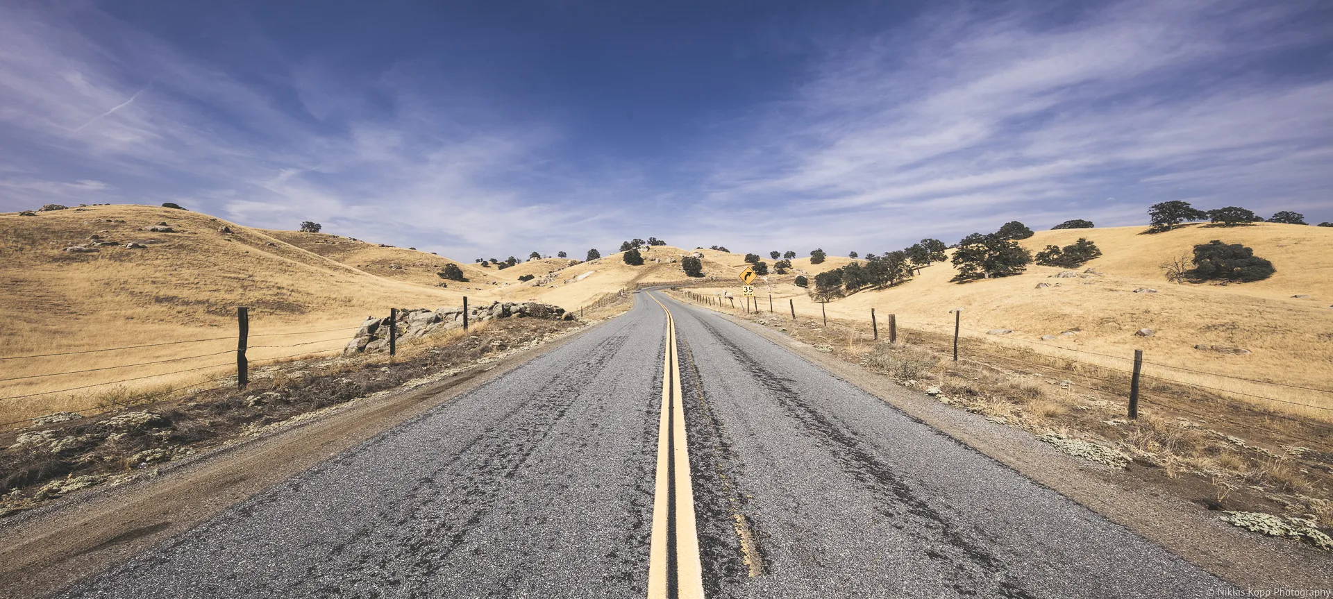 Eine leere Straße zieht als Fluchtlinie durch eine weite kalifornische Landschaft